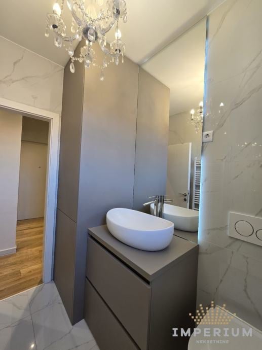 Modern bathroom with white oval vessel sink on gray vanity, crystal chandelier, marble tiles, and mirror