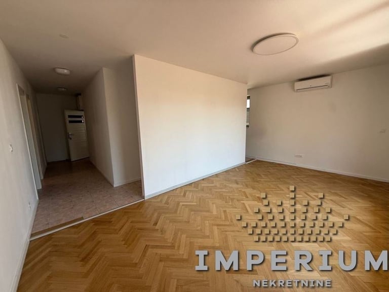 Empty apartment interior with herringbone wood flooring, white walls, and cardboard boxes arranged on floor