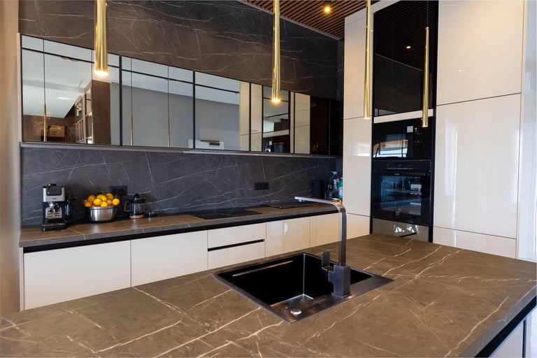 Modern kitchen with white cabinets, black marble backsplash, gold fixtures, and a central island with cooktop