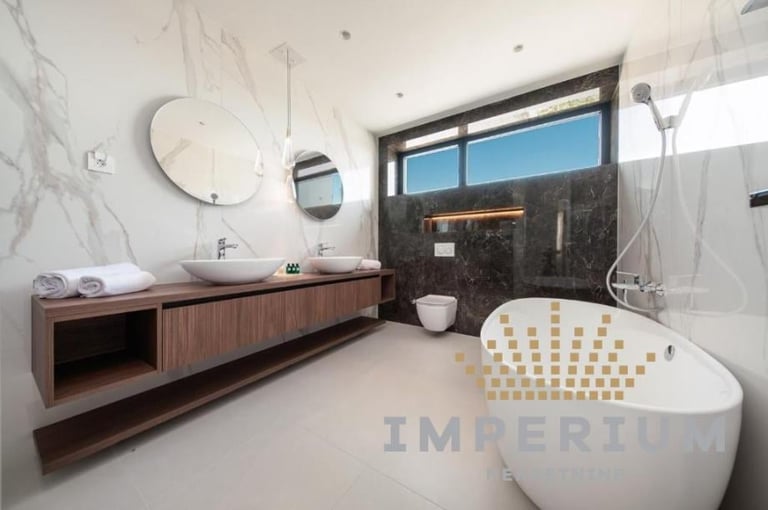 Modern luxury bathroom with freestanding white bathtub, wooden vanity, round mirrors, and large windows overlooking mountains
