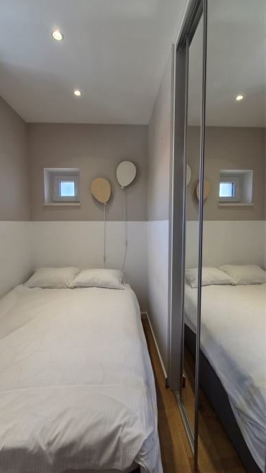 A narrow bedroom with a single bed, mirrored wardrobe, small windows, and decorative hanging balloons on the wall.