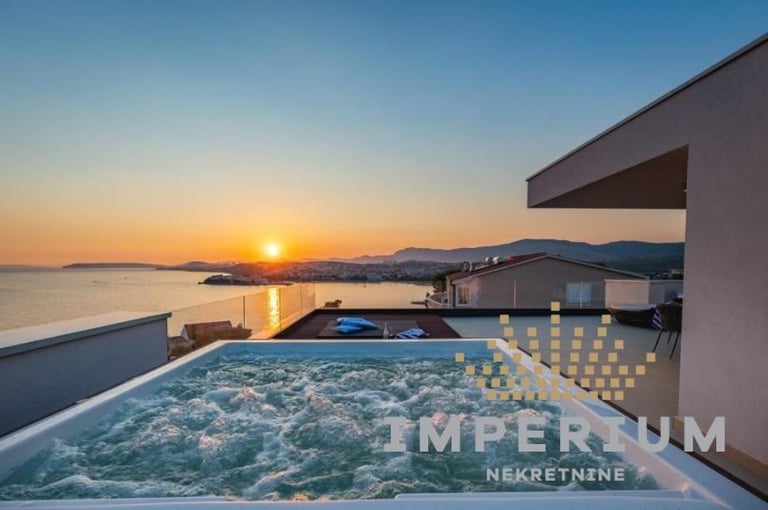 Luxury rooftop infinity pool at sunset overlooking the sea and mountains with a modern white villa