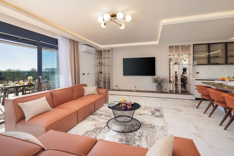 Modern living room with coral sofa, white marble flooring, wall-mounted TV, and open-plan kitchen with designer furnishings