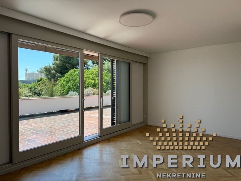 Modern apartment interior with large sliding glass doors opening to a terrace, wooden floor, and white walls with stacked boxes