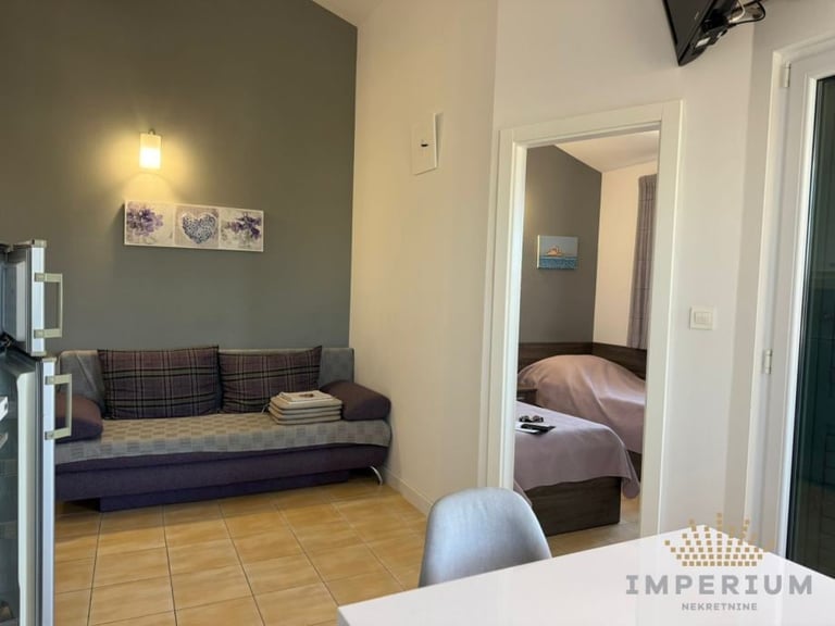 Modern studio apartment interior with gray walls, a sofa against the wall, open doorway to bedroom, and tiled flooring