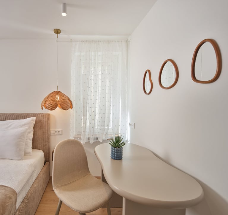 Modern bedroom with bed, white desk, beige chair, copper pendant lamp, and decorative oval mirrors on wall