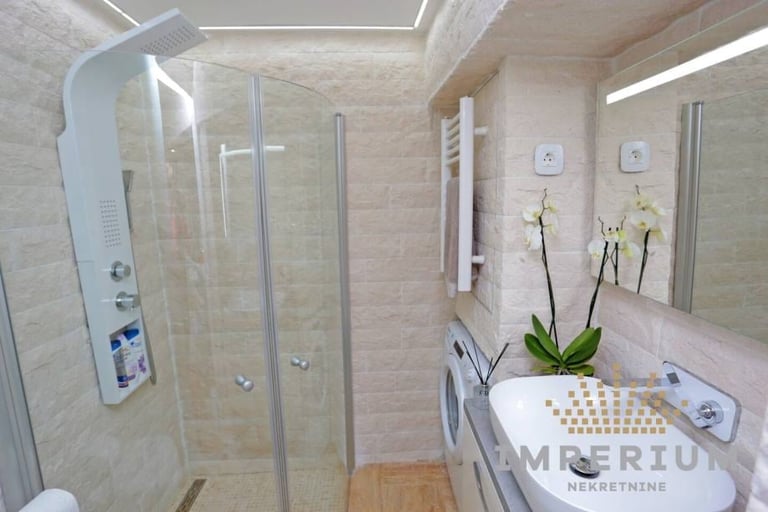 Modern bathroom with glass shower enclosure, white sink vanity, orchid plant, and light wood flooring
