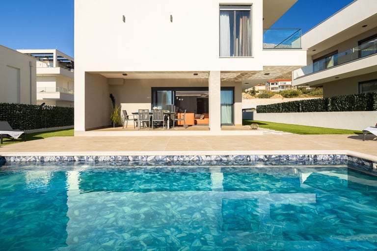 Modern white house with a swimming pool in the foreground, featuring a patio area and green lawn on a sunny day