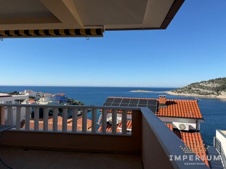 Balcony overlooking coastal Mediterranean town with terracotta roofs, blue sea, and hillside buildings under clear sky