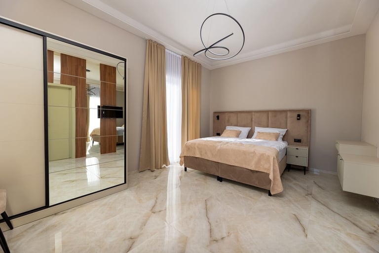 Modern bedroom with marble flooring, bed with beige linens, large mirror wardrobe, and contemporary pendant lighting