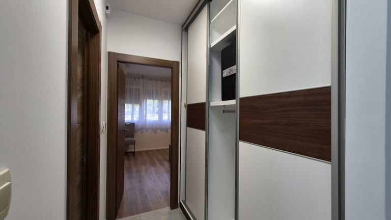 Modern hallway with white and dark wood wardrobe doors, leading to a living area with wooden flooring