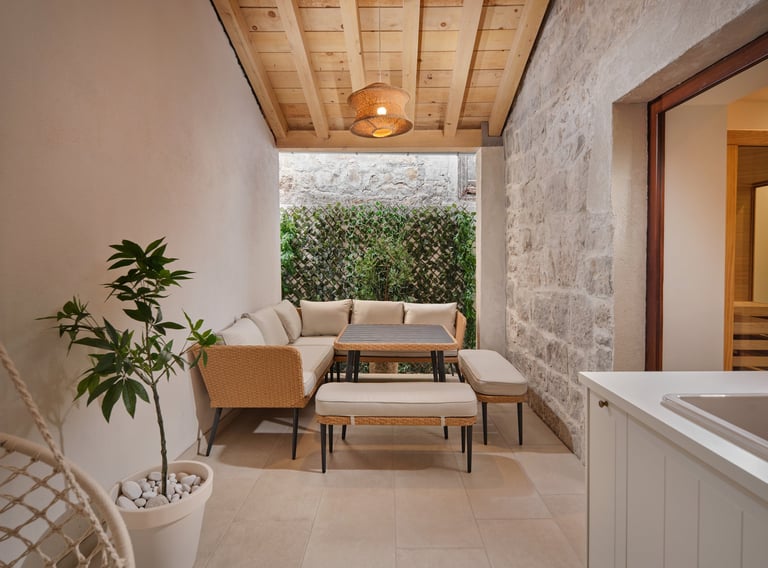 Modern patio lounge with beige seating, wooden ceiling, potted plant, and hedge backdrop