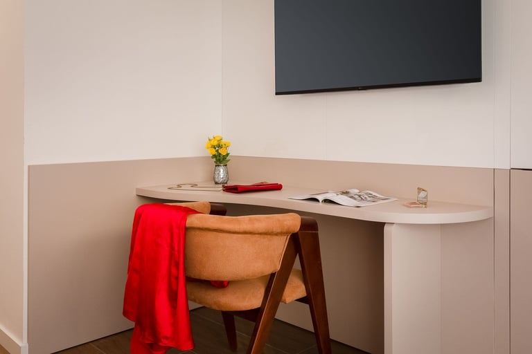 Modern minimalist workspace with wooden desk chair, red fabric, small yellow flower vase, and wall-mounted flat-screen TV above