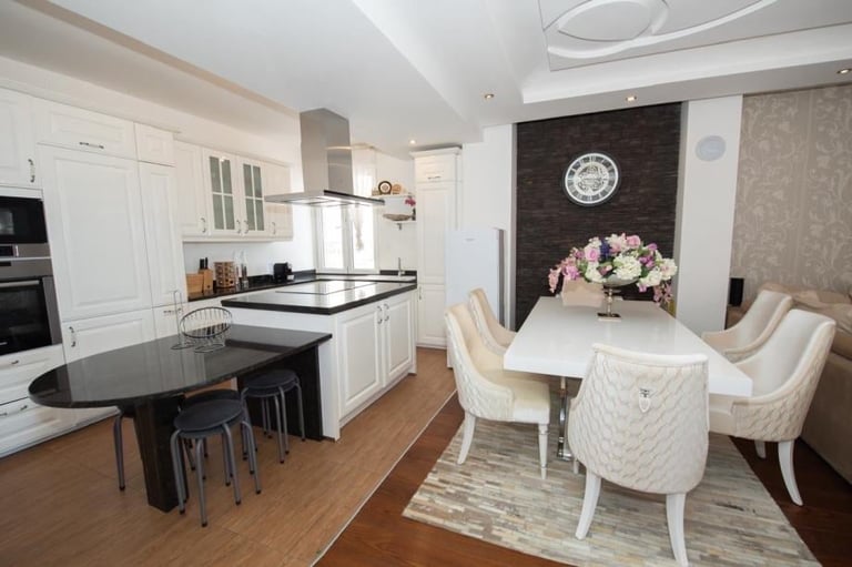 Modern open-concept kitchen and dining area with white cabinetry, black island, and cream dining chairs