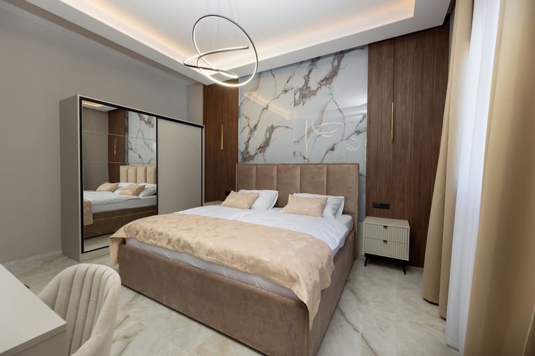 Modern bedroom with beige upholstered bed, mirrored wardrobe, marble flooring, pendant lighting, and marble-patterned accent wall
