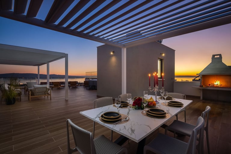 Modern rooftop dining area at sunset with set table, pergola, lounge seating, and ocean view in background