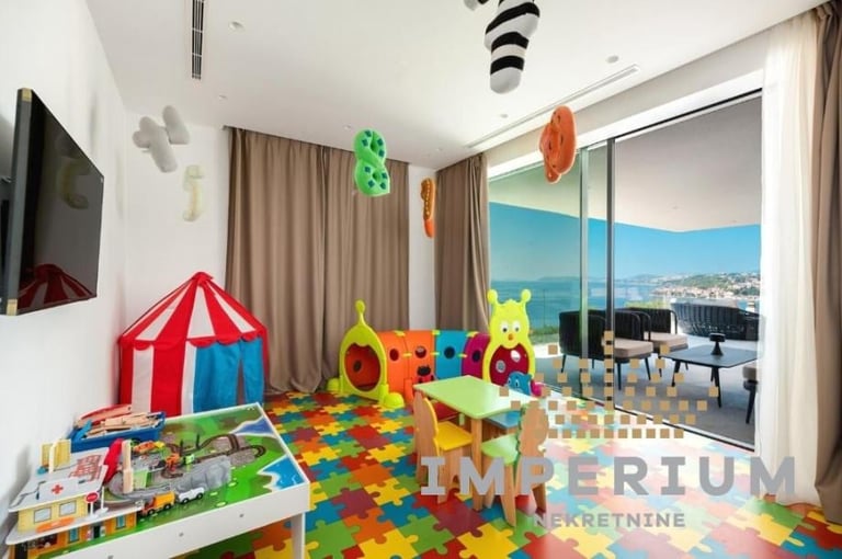 Colorful childrens playroom with a red and blue circus tent, toy tunnel, colorful foam mat, and ocean view through large windows.