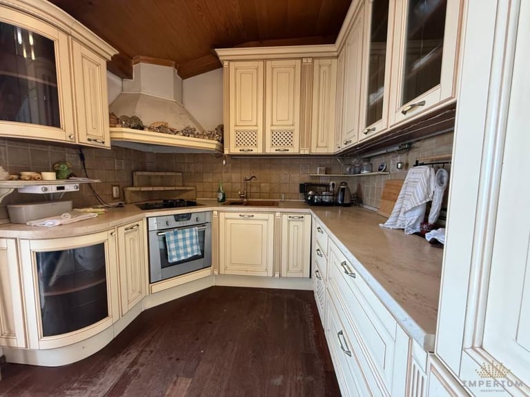 Modern cream-colored kitchen with L-shaped cabinetry, stainless steel appliances, dark countertops, and wood flooring