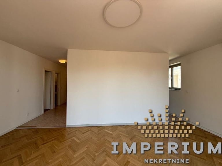 Empty apartment interior with herringbone wooden floor, white walls, stacked boxes, and Imperium Nekretnine watermark