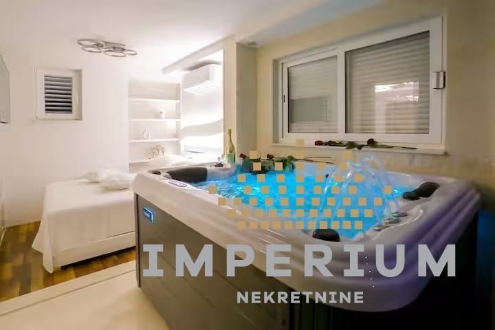 Modern spa bathroom with illuminated blue massage pool, white bed visible in background, and Imperium Nekretnine watermark