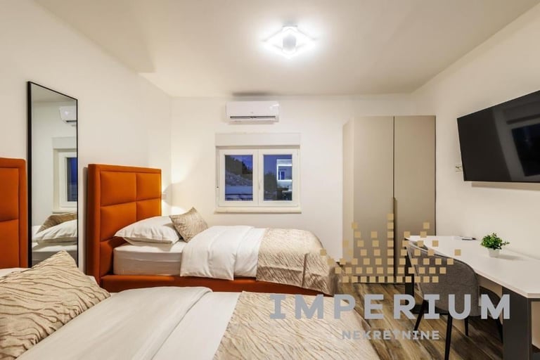 Modern hotel room with two beds, orange headboard, wall-mounted TV, and contemporary furnishings