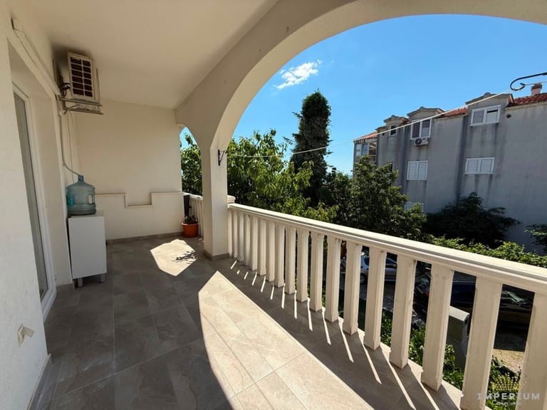 Spacious covered balcony with white railing overlooking residential area under clear blue sky