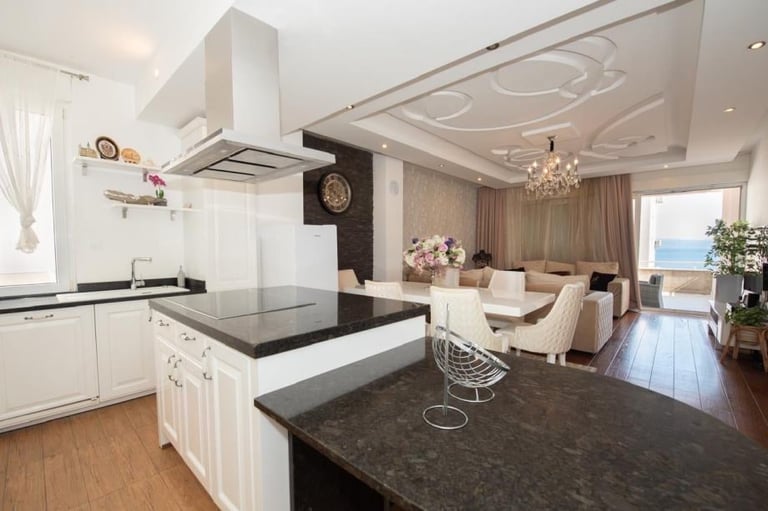 Modern open-concept kitchen and living room with white cabinetry, black granite island countertops, and ocean view windows