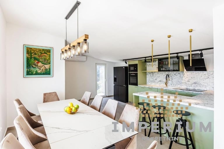 Modern kitchen and dining area with white table, brown chairs, pendant lighting, black and green cabinetry, marble backsplash, and bar seating