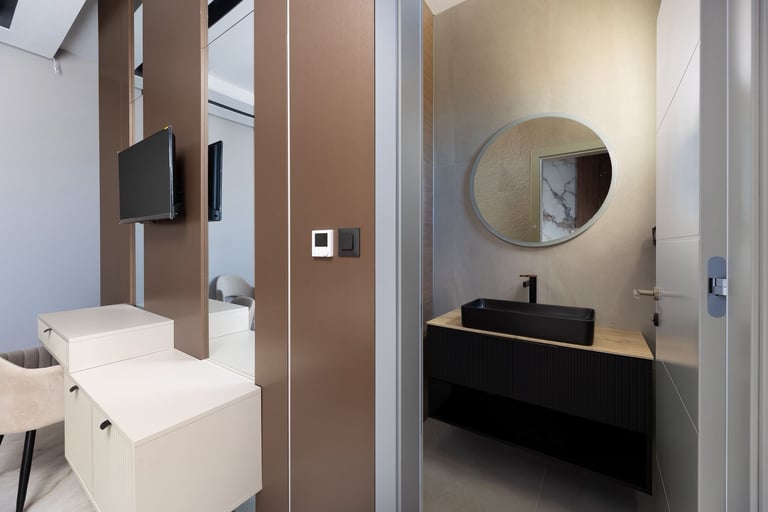 Modern bathroom with white toilet, white sink, black vanity with round mirror, and tan/brown partition wall dividing the space