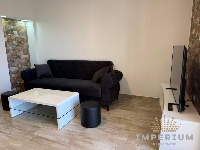 Modern living room with black sofa, white coffee table, black ottoman, and TV stand on wooden flooring