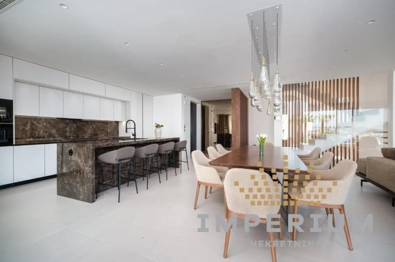 Modern open-plan apartment with white kitchen, dining area with patterned chairs, and living room with pendant lighting