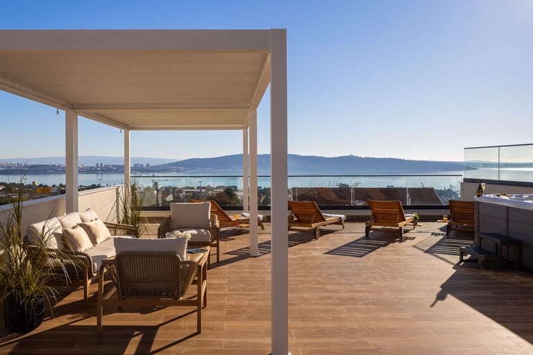 Modern rooftop terrace with wooden deck, shaded pergola, lounge furniture, and panoramic waterfront city views