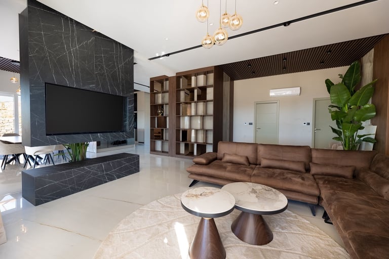 Modern living room with dark marble TV wall, brown sectional sofa, wood shelving, pendant lights, and decorative side tables with plant
