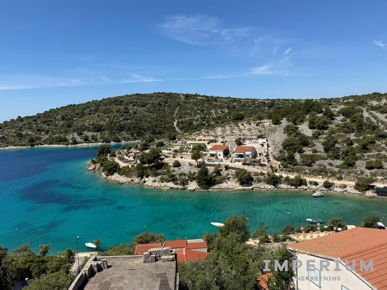 Coastal Mediterranean village with terracotta-roofed buildings nestled on a hillside above turquoise blue water
