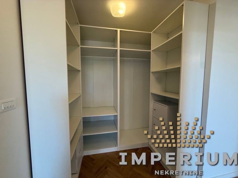 Empty walk-in closet with built-in shelving, hanging rods, and drawers, featuring white walls and modern design