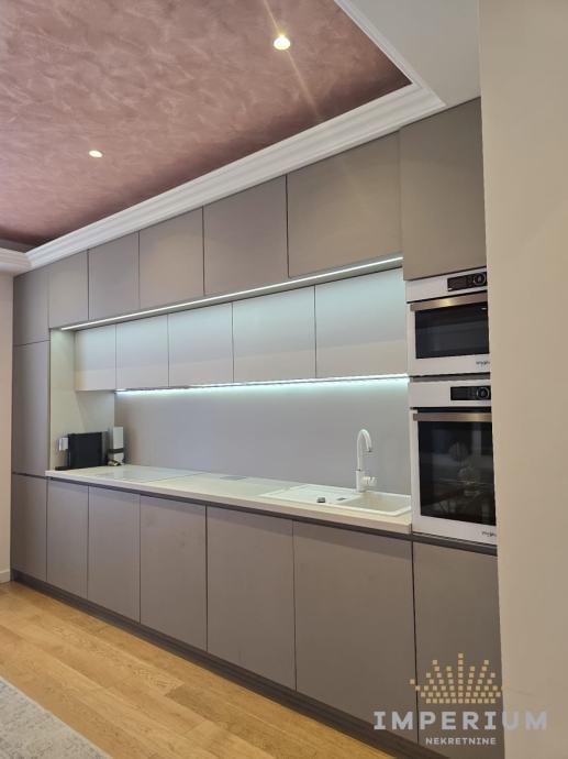 Modern gray kitchen with integrated appliances, white countertop, LED backlighting, and pink textured ceiling with recessed lights