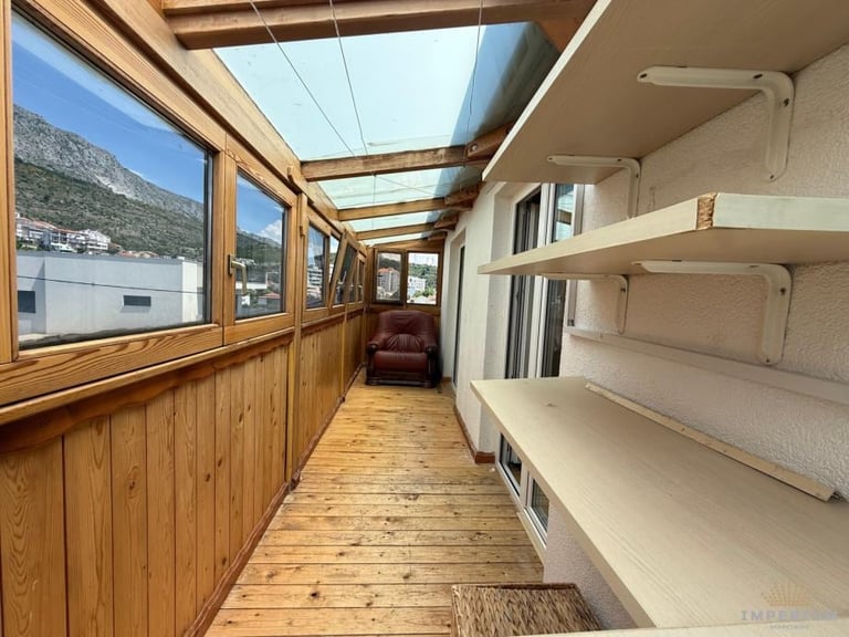 Interior of an RV or mobile home with wooden flooring, large windows, skylights, and built-in beige storage cabinets along one wall