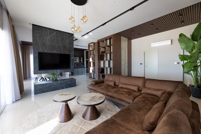 Modern living room with brown sectional sofa, black marble TV wall, wooden shelving, and minimalist furnishings bathed in natural light