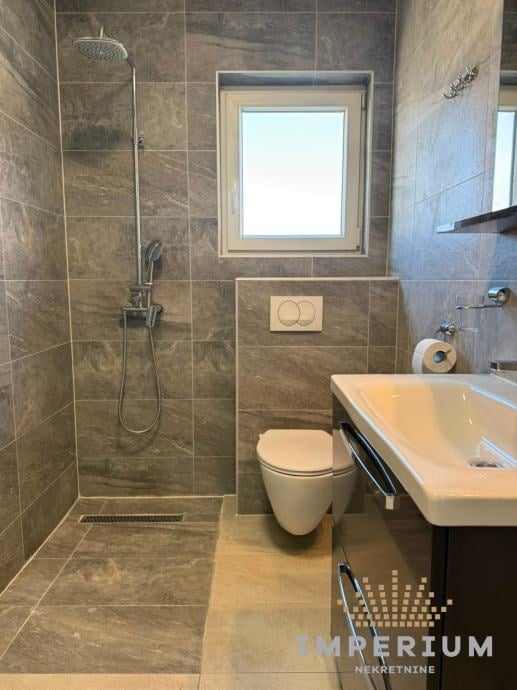 Modern bathroom with walk-in shower, wall-mounted toilet, vessel sink, and window with natural light