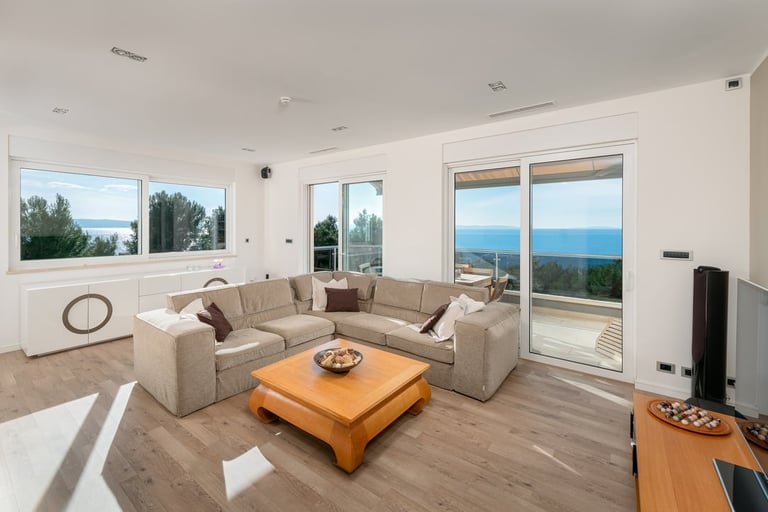 Modern living room with beige sectional sofa, wooden coffee table, and large windows overlooking mountain and water views