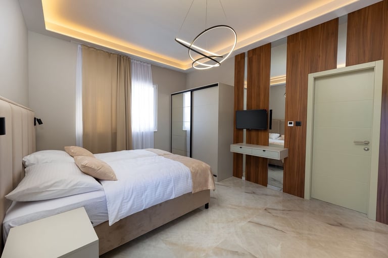 Modern bedroom with a gray bed, wooden wall panels, ceiling lighting, and marble flooring