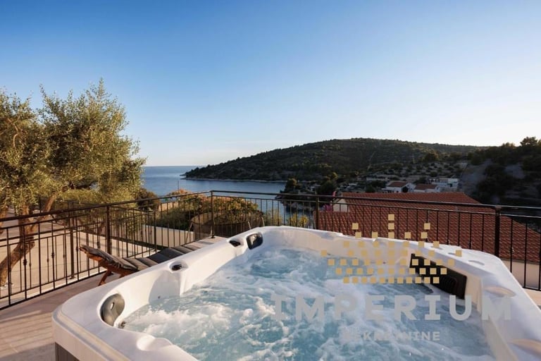 Hot tub on a wooden deck overlooking a scenic coastal bay with forested hills and calm blue water