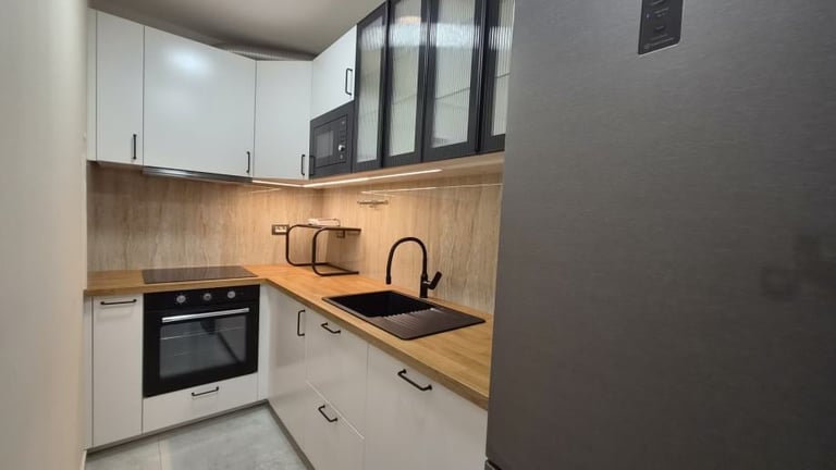 Modern compact kitchen with white cabinets, wood countertops, black oven, and stainless steel sink