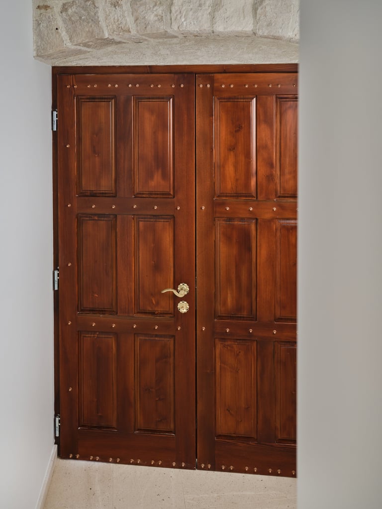 Large wooden double doors with six panels each, finished in rich mahogany-brown, with brass doorknob and white stone frame above