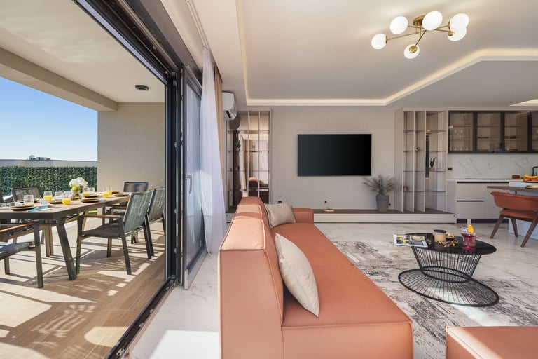 Modern living room with coral sofa, wall-mounted TV, and open terrace with dining area and scenic views