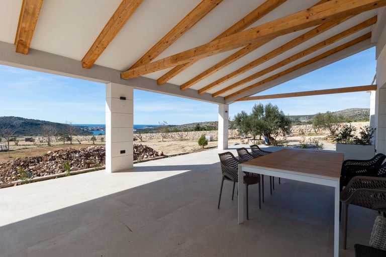 Modern covered patio with wooden beam ceiling, white concrete floor, dining furniture, and panoramic valley views