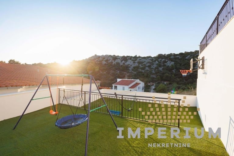 Modern backyard with childrens playground including swing set and trampoline on artificial grass at sunset