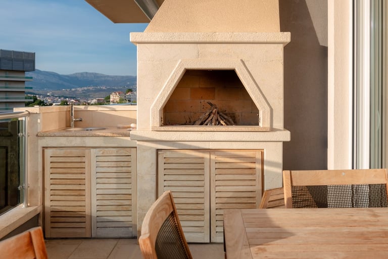 Rooftop fireplace with cream-colored exterior and wooden louvered cabinets below, overlooking city and mountains