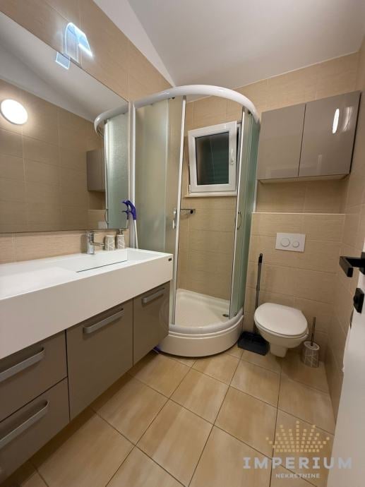 Modern bathroom with beige tiles, white vanity sink, curved glass shower enclosure, and toilet