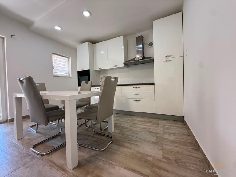 Modern kitchen and dining area with white cabinets, stainless steel appliances, white table, and gray chairs on wood flooring